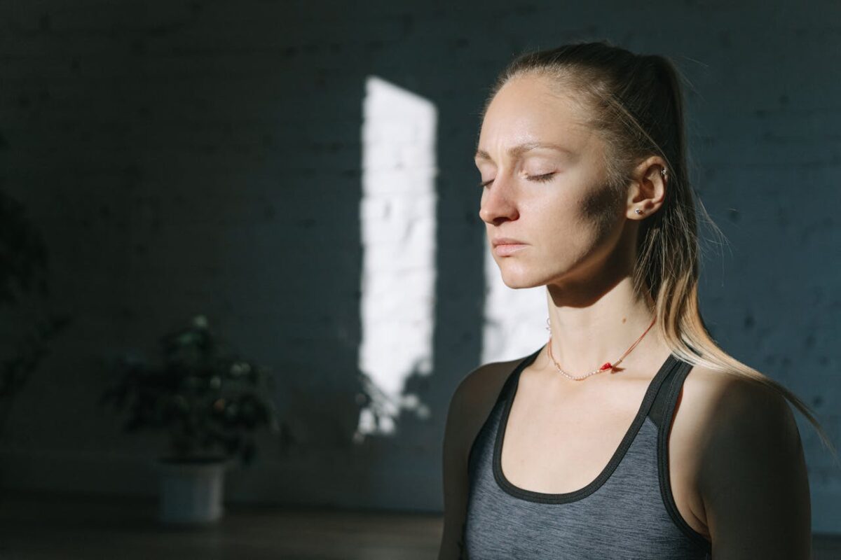 A woman in meditation inside a sunlit room, eyes closed, feeling calm and peaceful.