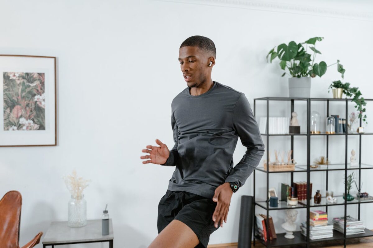 Man working out at home, wearing earbuds, surrounded by modern decor and lush plants.